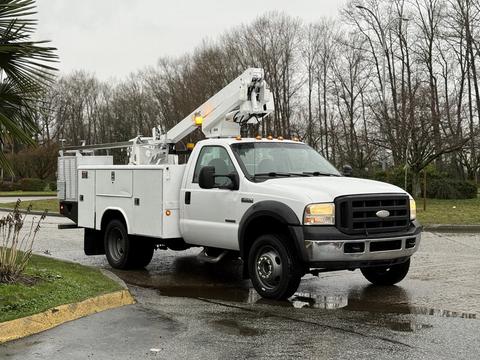 A white 2006 Ford F-450 truck with an elevated work platform and a toolbox mounted in the bed