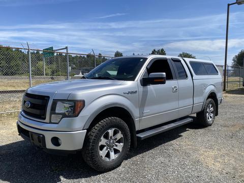 A silver 2014 Ford F-150 with a truck bed cover parked at an angle displaying its front and side features including large wheels and chrome accents