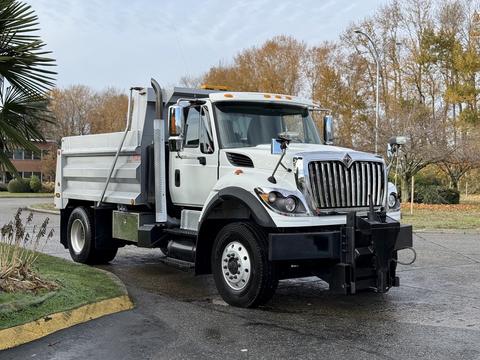 A 2011 International WorkStar truck with a white cab and a silver dump bed is parked with its plow attached in the foreground