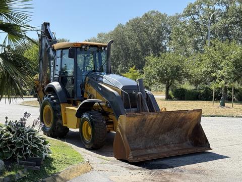 A 2013 John Deere 710K backhoe loader with a large front bucket and rear excavator arm positioned on a roadway
