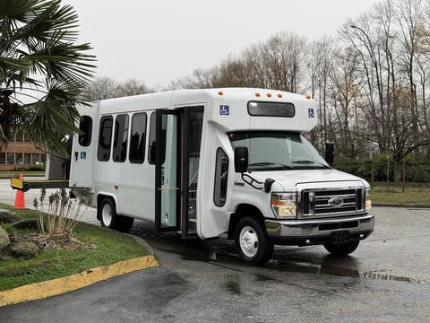 A 2017 Ford E450 shuttle bus with a white exterior and accessible features parked at an angle with its side door open