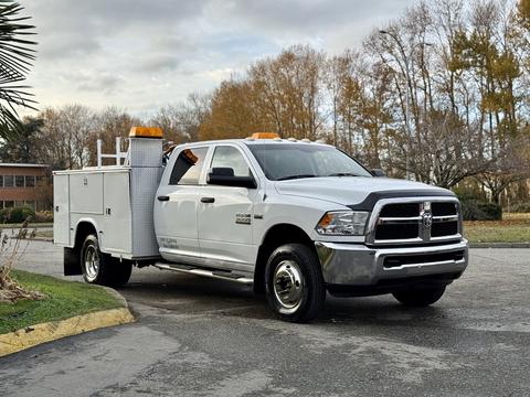 A 2013 RAM 3500 white pickup truck with a storage box on the bed and orange lights on top parked on a road