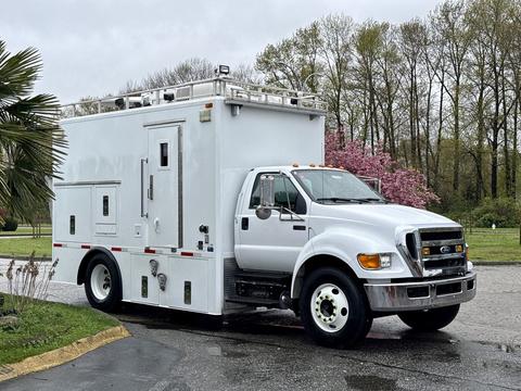 A white 2011 Ford F-650 with a large cargo area and an equipment box on the back designed for utility or service purposes