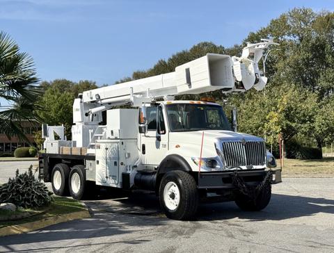 A white 2006 International 7500 truck with an extended hydraulic boom and an equipment bed is parked on a paved area