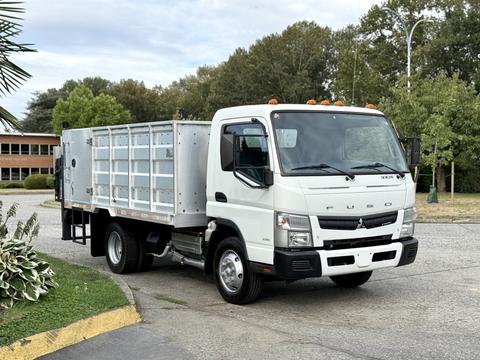 A 2014 Mitsubishi Fuso FE truck with a flatbed and metal side rails parked at an angle