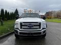 A 2016 Ford F-550 with a white exterior and a flatbed, featuring a prominent front grille, headlights, and multiple orange lights on the roof