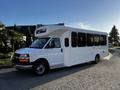 A white 2017 Chevrolet Express shuttle bus with large windows and a high roof is parked on a road