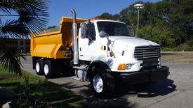 A white 2007 Sterling LT8500 dump truck with a bright yellow bed and large tires parked in a lot