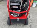 A red Magnum 4000 Hot Water Pressure Washer with a black engine and hoses attached, featuring wheels for mobility and a sturdy frame