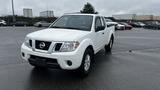 A white 2016 Nissan Frontier pickup truck parked on a lot with visible front headlights and a distinctive grille design