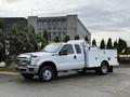 A white 2013 Ford F-350 SD truck with a utility bed and toolboxes on the side parked on a driveway