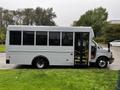 A 2015 Chevrolet Express bus with large windows and an open door on the side parked on grass