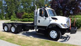 A white 2013 International 7400 Workstar truck with a large chrome exhaust pipe and dual rear wheels parked on a grassy area