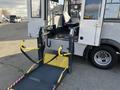 A 2018 Chevrolet Express van with a fold-out wheelchair lift positioned at the entrance, featuring safety straps and yellow handlebars