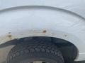 A close-up of the wheel arch of a white 2009 Ford F-150 showing some rust and a black tire with textured tread pattern