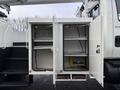 A white utility storage compartment with two open doors revealing shelves and a battery inside