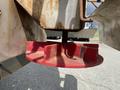 A close-up view of a red circular plow blade attached to the underside of a rusted metal frame