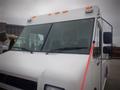 A white 2003 Freightliner MT45 Chassis delivery vehicle with a large windshield and multiple orange lights on the roof