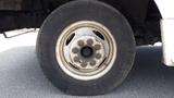 A close-up of a 2011 Ford Econoline wheel showing a dirty tire and a silver metal rim with eight lug nut holes