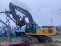 A yellow and black 2014 John Deere 350G excavator with a large digging arm and tracks sits in a construction area