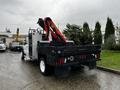 A white 2014 Ford F-550 flatbed truck with a mounted crane attachment on the back