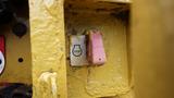 Close-up of a yellow control panel with a red and white stop button and a pink button beside it, mounted on a heavy machinery unit