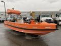 A 2008 Fassmer 20 Foot Fast Rescue boat in bright orange color featuring a covered seating area and a console with steering wheel and controls