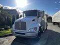 A 2013 Kenworth T370 truck with a white body and distinctive grille design is facing the viewer with its headlights on and a shining hood ornament