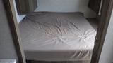 A neatly made bed with a beige fitted sheet in a camper interior with wooden cabinets above