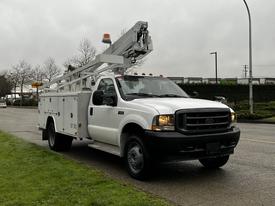 A white 2004 Ford F-450 SD with a utility body and a telescoping aerial lift is parked on the side of the road