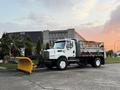 A white 2006 Freightliner M2 106 truck with a yellow snowplow attachment in front of a large building