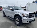 A silver 2014 Ford F-150 with chrome wheels and a bed cap parked at an angle showcasing its front grille and headlights