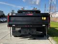 A black 2021 Ford F-550 flatbed truck viewed from the rear with a logo on the tailgate and visible chains hanging down from the bumper