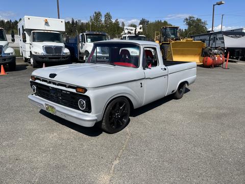A 1962 Ford F-100 pickup truck with a gray body and black rims parked in a lot showing a classic design and vintage style