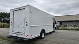 A white 2006 Ford Econoline van with a boxy cargo area and a roll-up rear door parked on gravel