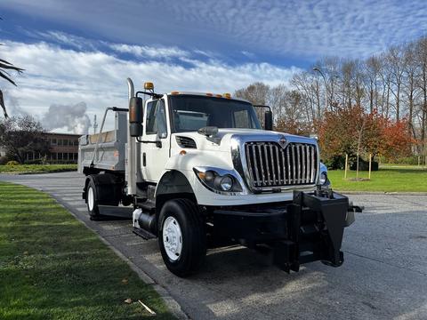 A 2011 International 7500 truck with a white cab and black grill parked on the road featuring a flatbed and snow plow attachment in the front