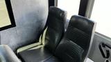 A pair of dark leather seats inside a bus with textured upholstery and a sleek design