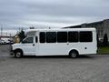 A white 2017 Chevrolet Express with a shuttle bus design, featuring large windows and a raised roof, parked on a gray surface