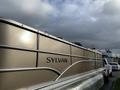 A 2013 Sylvan pontoon boat with a silver exterior and the name "SYLVAN" prominently displayed on the side