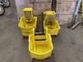 Ten yellow mop buckets with wringers and assorted brooms arranged in a group