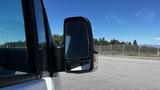 A side mirror of a 2016 Mercedes-Benz Sprinter reflecting a clear blue sky