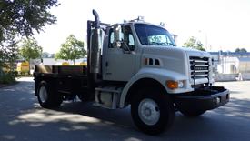 A white 2007 Sterling Acterra L7500 truck with a flatbed and visible chrome accents parked on a road