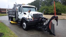 A 2010 International 7400 truck with a snow plow attached to the front and a dump bed in the back painted white and black