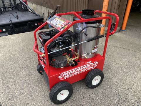 A red Magnum 4000 Hot Water Pressure Washer on four wheels with a metal tank and various attached hoses and controls