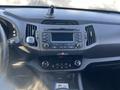 The interior dashboard of a 2012 Kia Sportage featuring a central display screen and controls for audio and climate settings