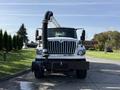 A white 2013 International 7400 truck with a large black vacuum hose attached to the front facing forward