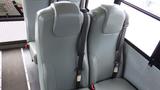 Interior view of two green upholstered bus seats with safety belts secured in an upright position