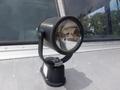 A black spotlight mounted on a bracket with a round reflective surface and a base, designed for use on a vehicle