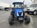 A blue 2007 New Holland TN70A tractor with a cab and large rear tires facing forward in a parking area