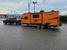 A 2015 Winnebago of Indiana travel trailer in bright orange color being towed by a black pickup truck